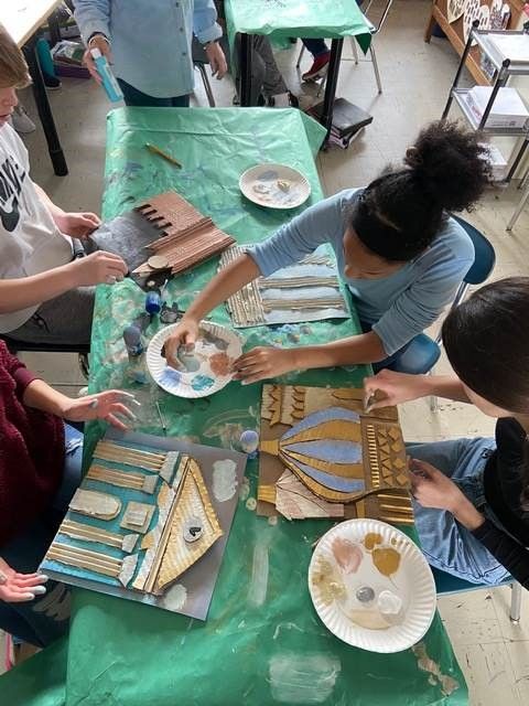 several people are sitting at a table making decorative paper plates with gold and silver designs on them