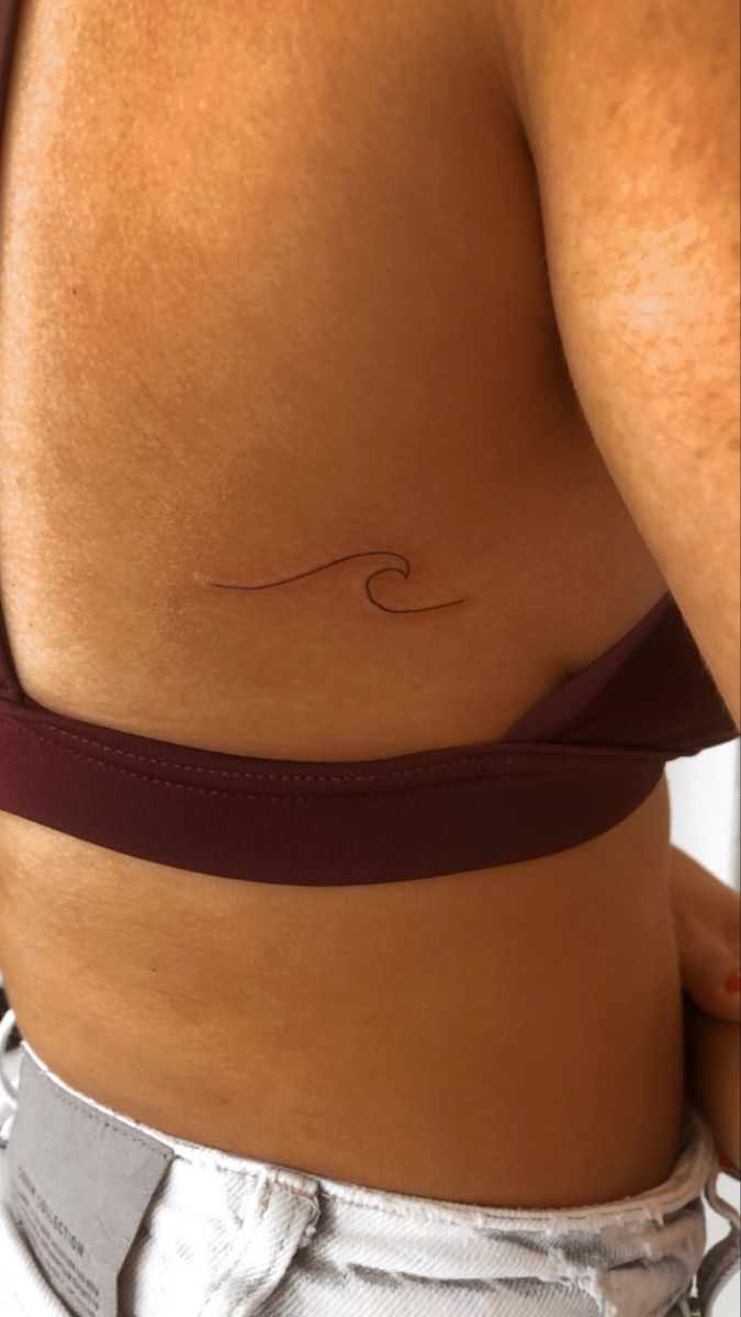 a woman's stomach with a small wave tattoo on her left side ribcage