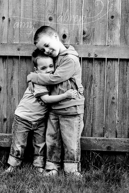 two young boys hugging each other in front of a fence