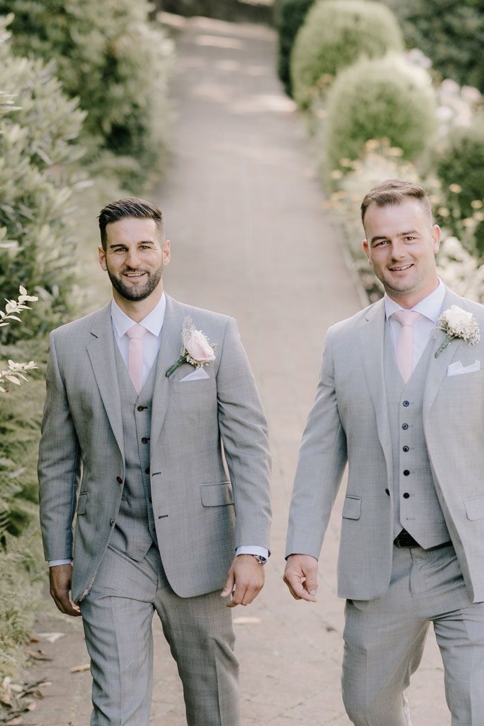 two men in grey suits walking down a path together, one is holding the other's hand