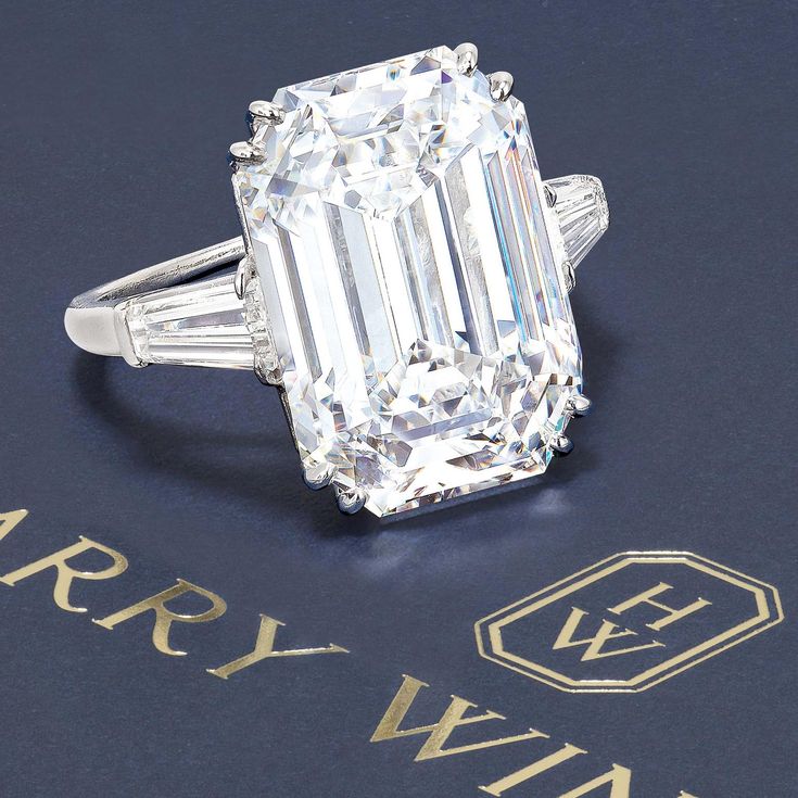 an emerald - cut diamond ring with baguettes and tapered sidestones sits on a blue surface