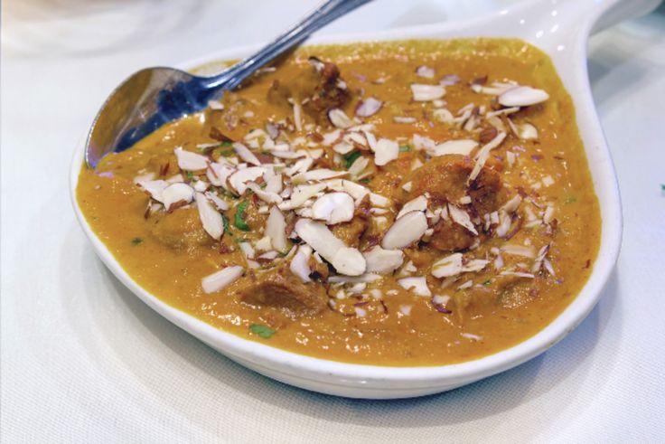 a white bowl filled with food on top of a table next to a silver spoon