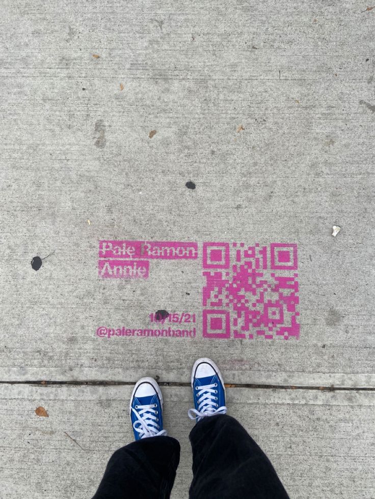 someone is standing on the sidewalk with their feet in blue and white sneakers, next to a pink qr code