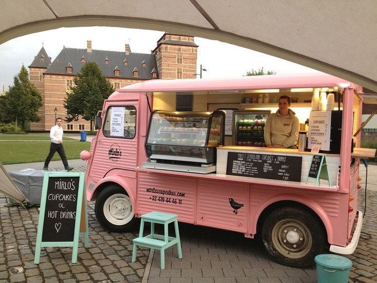 a pink food truck parked on the side of a road next to a building with a man standing behind it