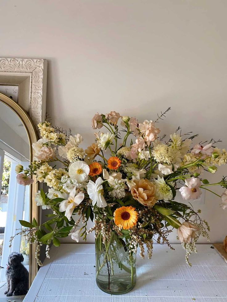 a vase filled with lots of flowers sitting on top of a table next to a mirror