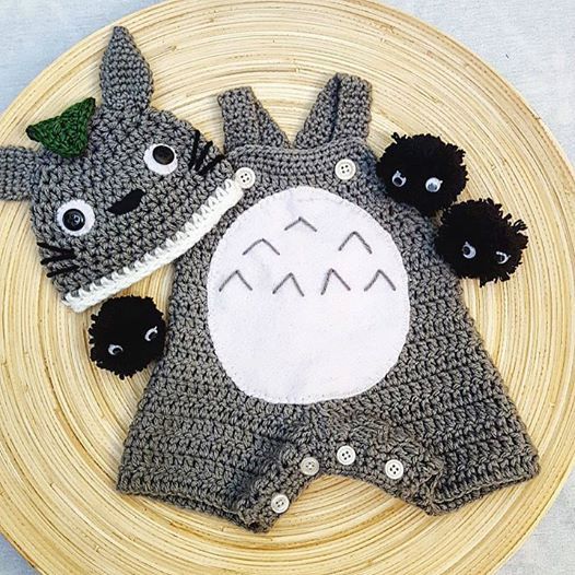 a crocheted baby bib and hat on a plate with black pom poms