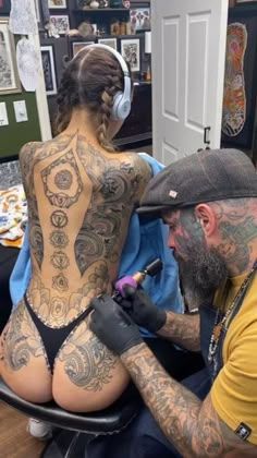 a tattooed man getting his tattoo done by a woman in a yellow shirt and black hat