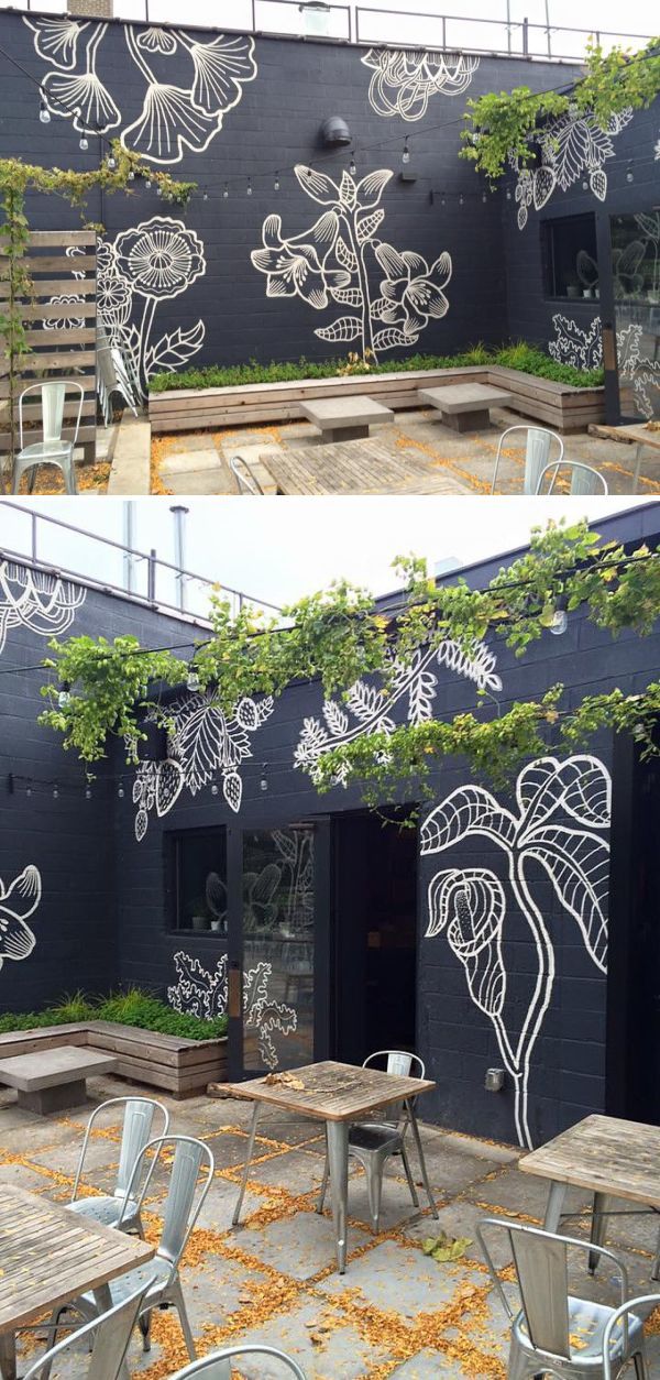 an outdoor dining area with tables and chairs painted on the side of a black building