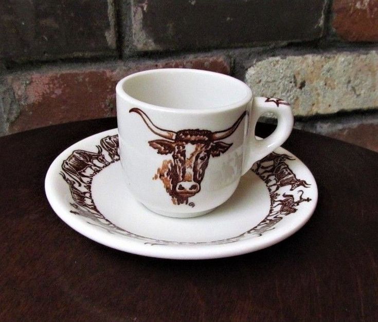 a coffee cup and saucer with a bull design on the side sitting on a wooden table