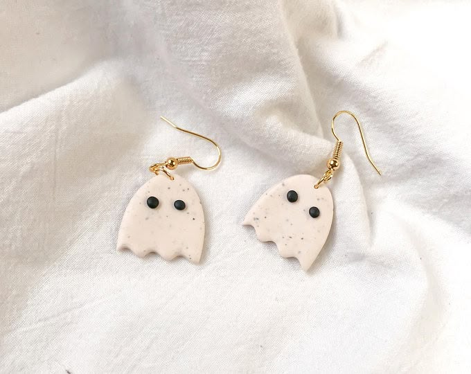 two white ghost earrings with black eyes and gold earwires on a white cloth