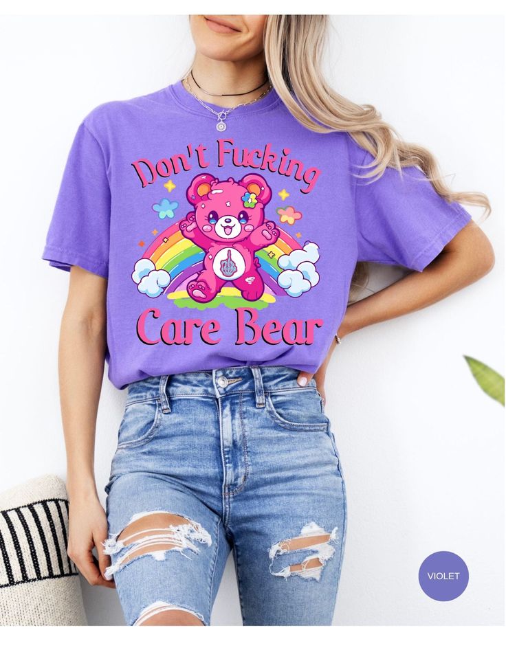 Indulge in rebellious comfort with our "I Don't Care Bear Vibes" T-shirt! This whimsical tee features a cheeky care bear boldly expressing your carefree attitude with a pair of unmistakable middle fingers and a vibrant rainbow backdrop. Crafted from soft, breathable fabric, this shirt guarantees both style and comfort. Embrace the carefree spirit and make a statement with this playful addition to your wardrobe. It's not just a shirt; it's an expression of your "don't give a care" attitude! *Unisex Sizing* Trendy Crew Neck T-shirt With Bear Print, Fun Purple T-shirt With Funny Print, Casual Purple T-shirt With Cartoon Print, Playful Cotton Tops With Bear Print, Cute Short Sleeve T-shirt With Bear Print, Casual Short Sleeve T-shirt With Bear Print, Bear Print Crew Neck T-shirt For Streetwear, Crew Neck T-shirt With Bear Print For Streetwear, Cute Bear Print Crew Neck T-shirt