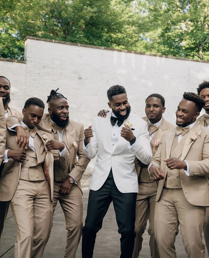 a group of men standing next to each other wearing tan suits and bow ties with trees in the background