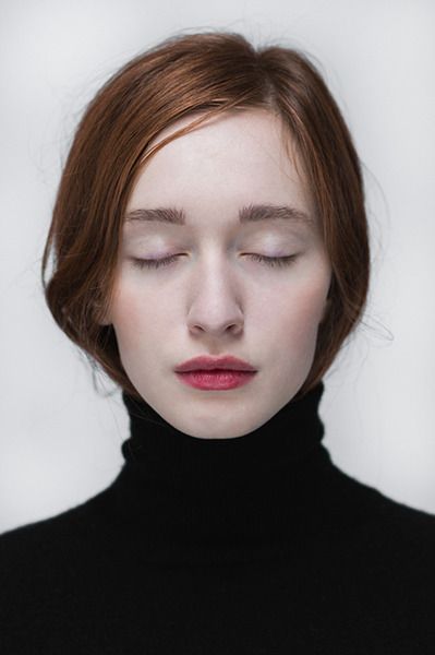 a woman with her eyes closed wearing a black turtle neck top and red hair is staring at the camera