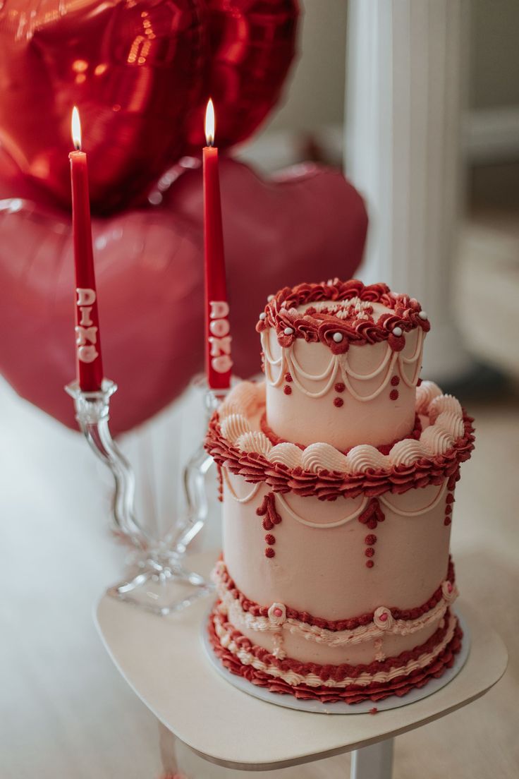 two tiered cake sitting on top of a table next to red balloons and candles