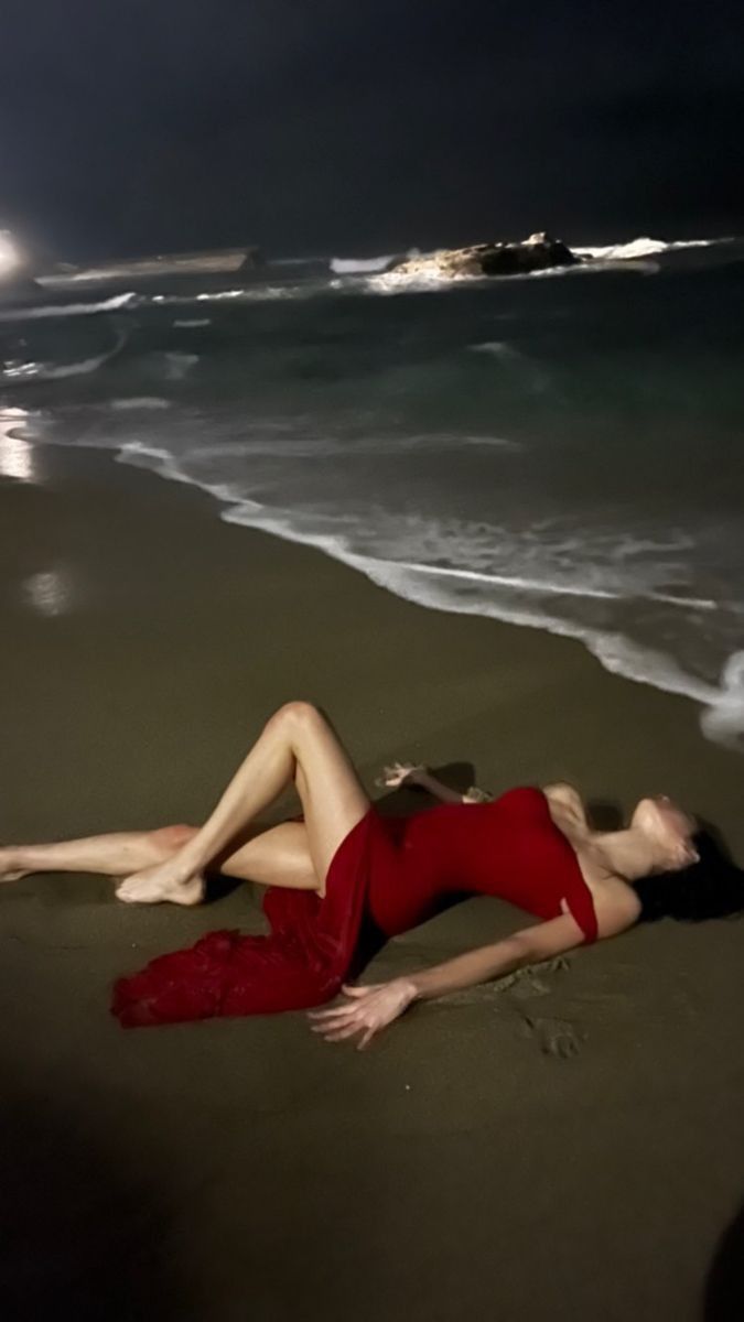 a woman laying on top of a sandy beach next to the ocean under a full moon