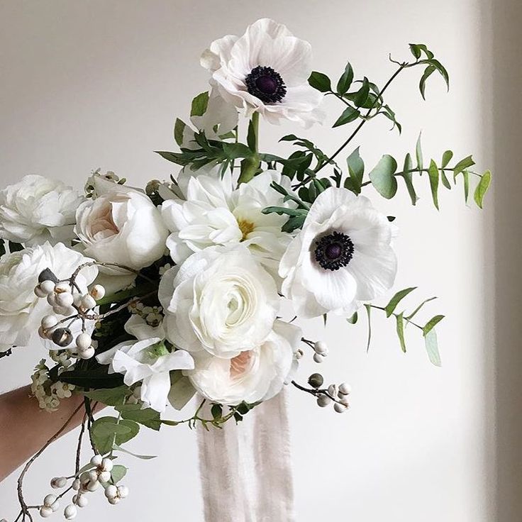 a woman holding a bouquet of white flowers in her hand with greenery on the side