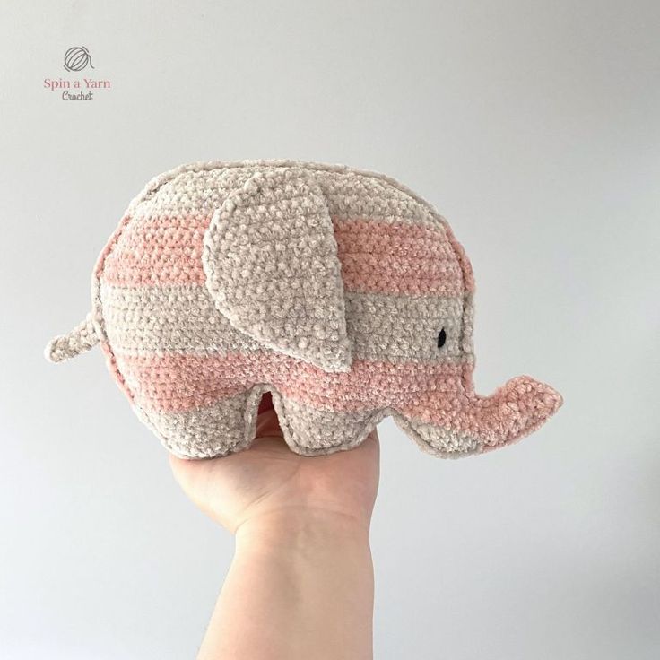 a hand holding up a small crocheted stuffed elephant with pink and white stripes