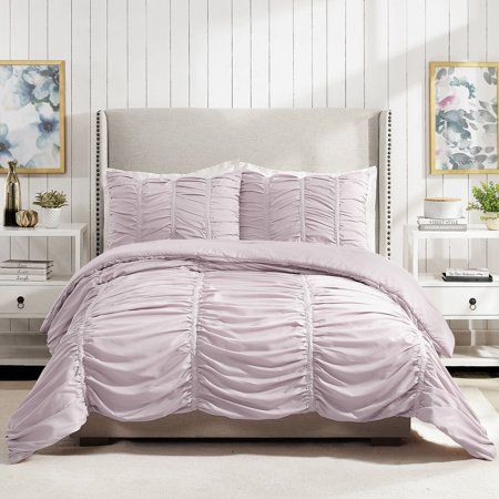 a bed with pink comforter and pillows in a white room next to two nightstands