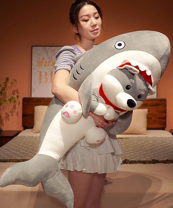 a woman is holding a stuffed shark and dog in her arms while standing on a bed