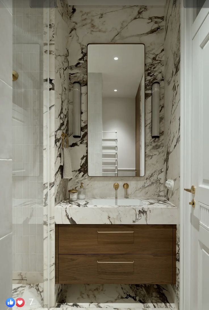 a bathroom with marble walls and flooring is pictured in this image, there is a mirror on the wall above the sink