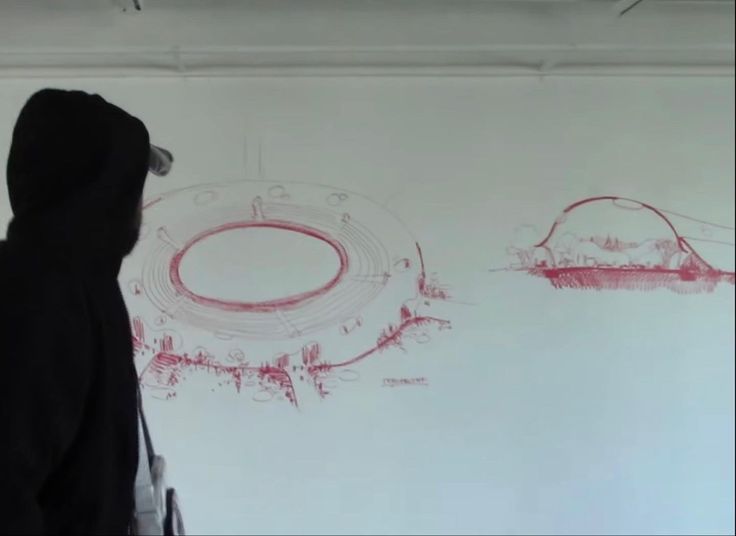 a person standing in front of a white wall with red drawings on it and a black hoodie