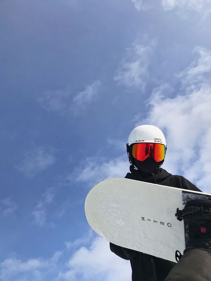 a snowboarder holding his board under a blue sky with clouds in the background