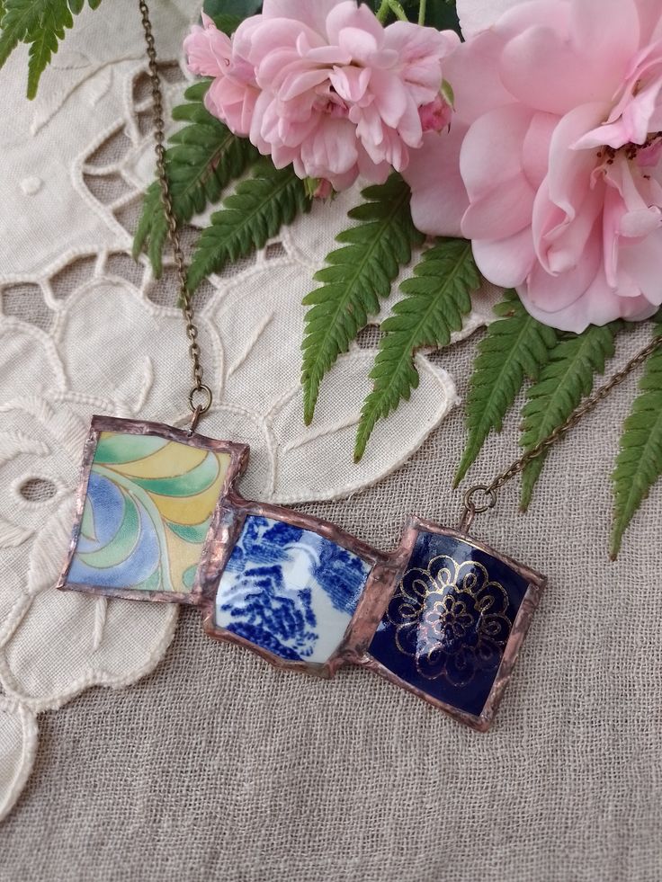 three necklaces with flowers and leaves on a lace doily next to pink carnations