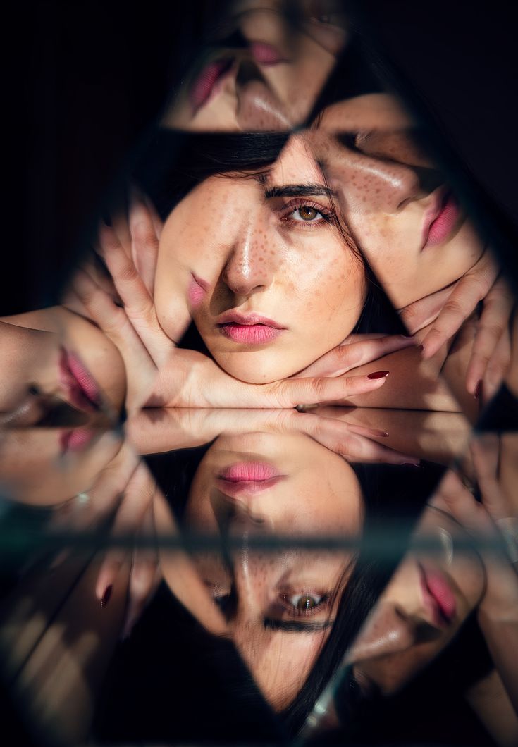 a woman with her hands on her face looking at the camera through a glass mirror