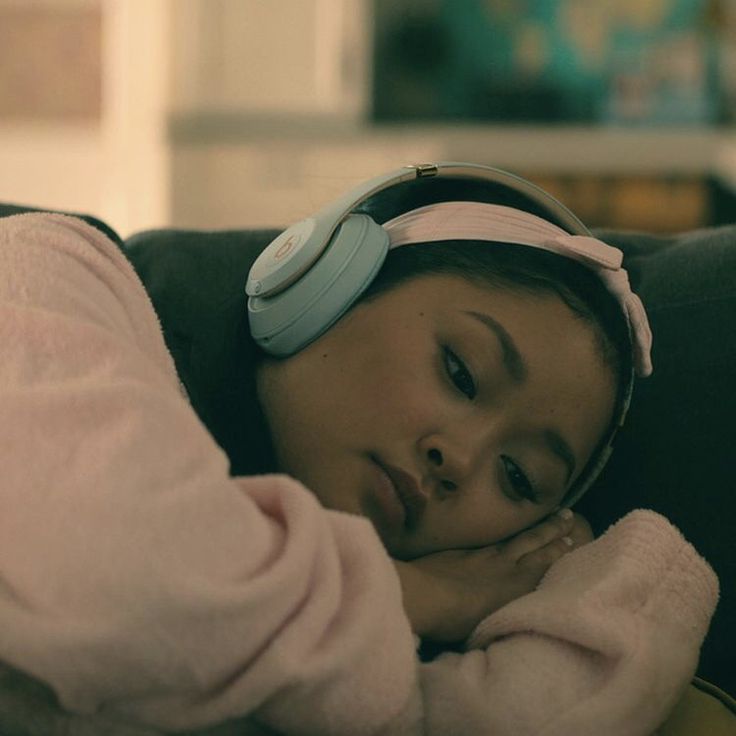 a woman laying on top of a couch wearing headphones and listening to music with her eyes closed