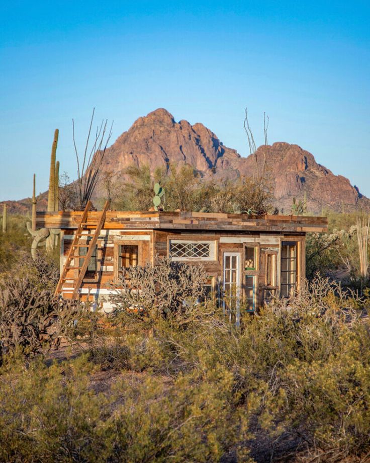 an old building in the desert with mountains in the backgrouds and cactus trees