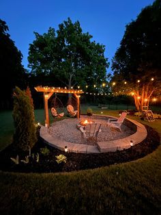 an outdoor fire pit in the middle of a yard at night with string lights strung around it