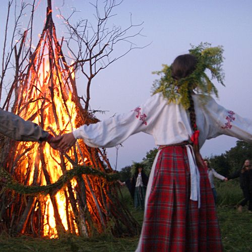 two people holding hands in front of a burning teepeel at dusk with other people standing around