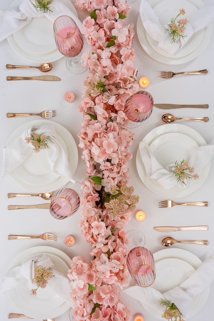 the table is set with pink flowers and gold place settings for an elegant dinner party