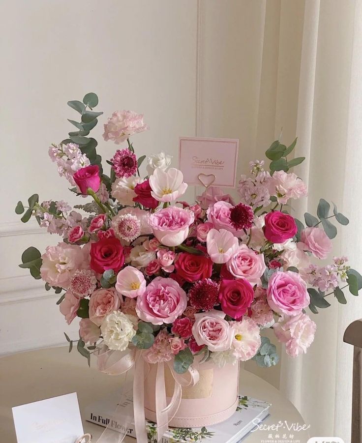 a bouquet of pink and white flowers sitting on top of a table next to a card