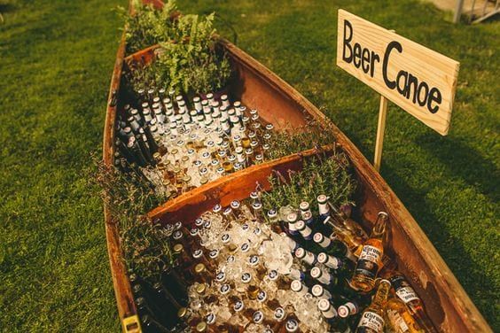 a wooden boat filled with beer bottles on top of a lush green field next to a sign that says deer dance