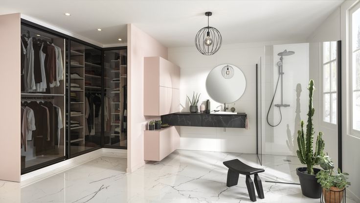 a walk in closet filled with lots of clothes next to a mirror and potted plant