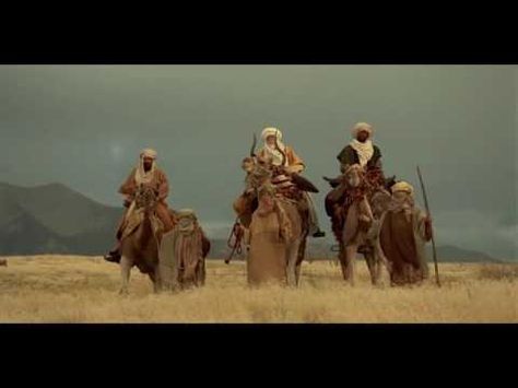 three men riding on the backs of camels in an open field with mountains in the background