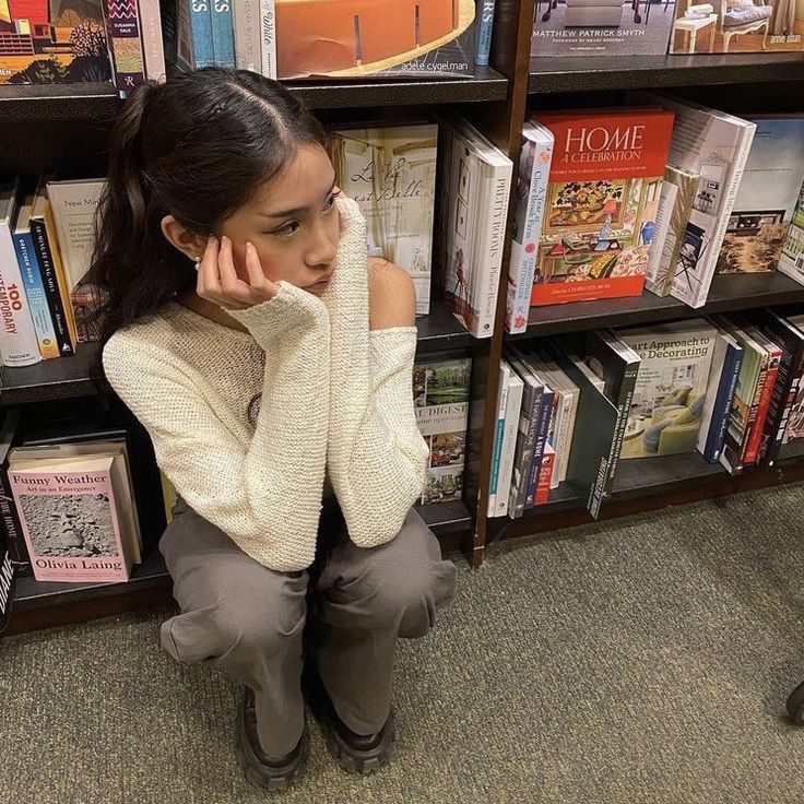 a woman sitting on the floor in front of a book shelf with books behind her