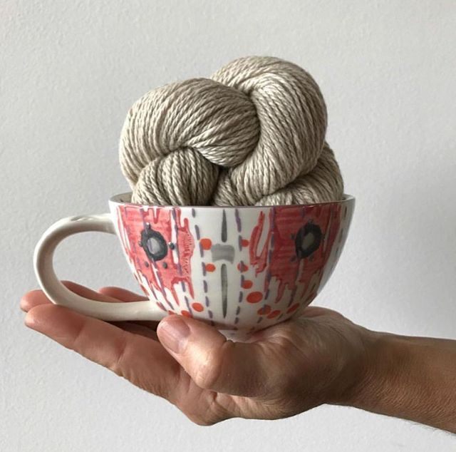 a hand holding a cup with yarn in it