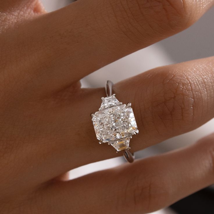 a woman's hand with a diamond ring on top of her finger and the other hand holding an engagement ring