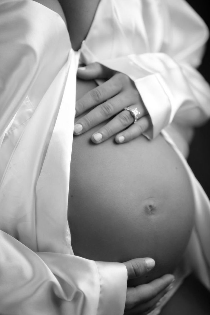 a pregnant woman in white shirt and tie holding her belly up to the side with both hands