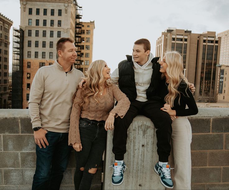 three people sitting on top of a stone wall with buildings in the backgroud