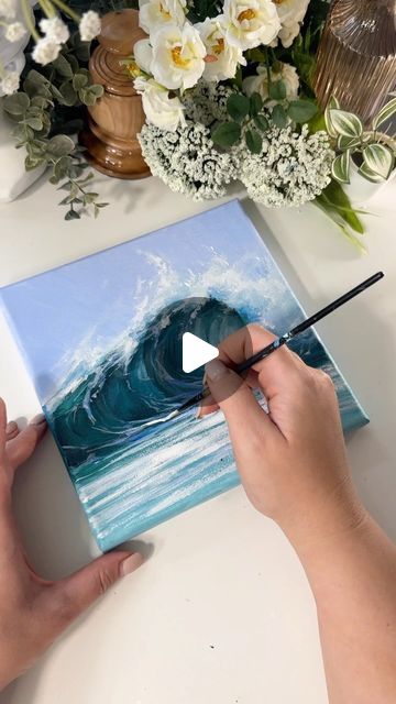 someone is painting an ocean scene with white flowers