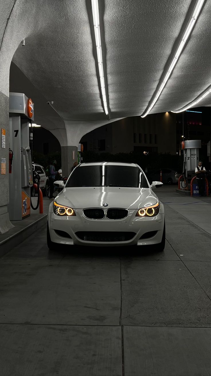 a white car is parked in a parking garage with its lights on and it's hood up