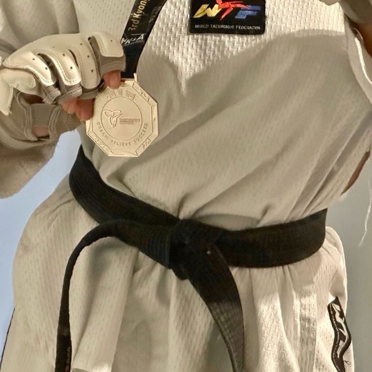 a person wearing a white uniform and black belt holding a silver medal in their right hand