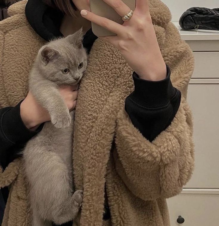 a woman taking a selfie with her cell phone while holding a cat in her arms