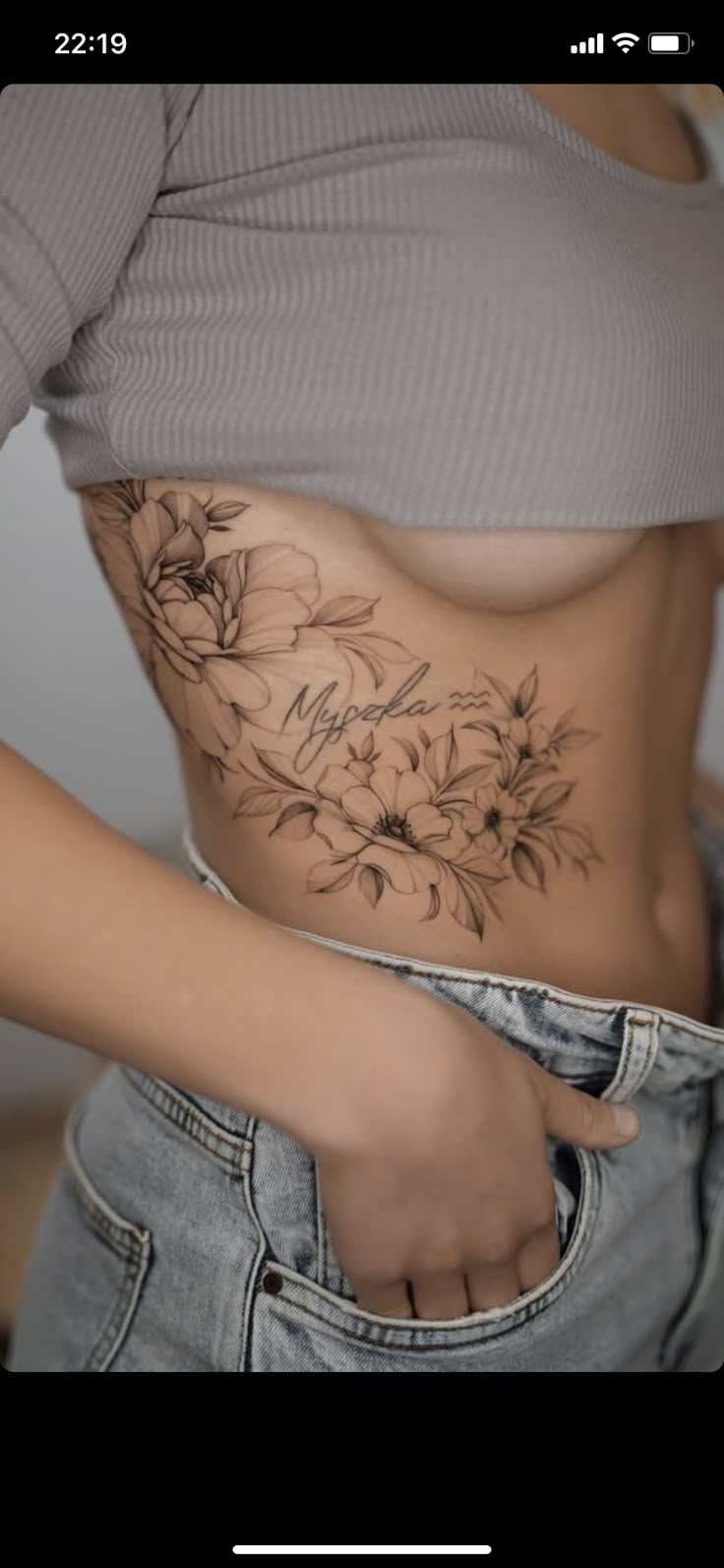 a woman's stomach with flowers tattooed on the side and her hand in her pocket