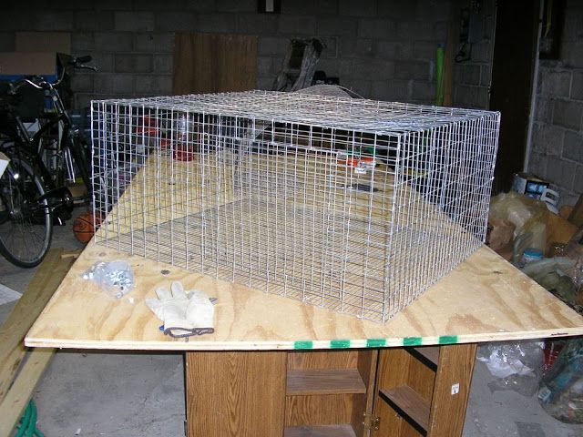 a bird cage sitting on top of a wooden table next to a bike in a garage