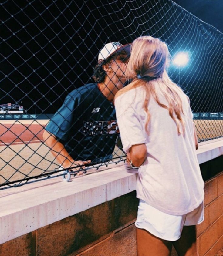 a man and woman standing next to each other near a tennis court net at night