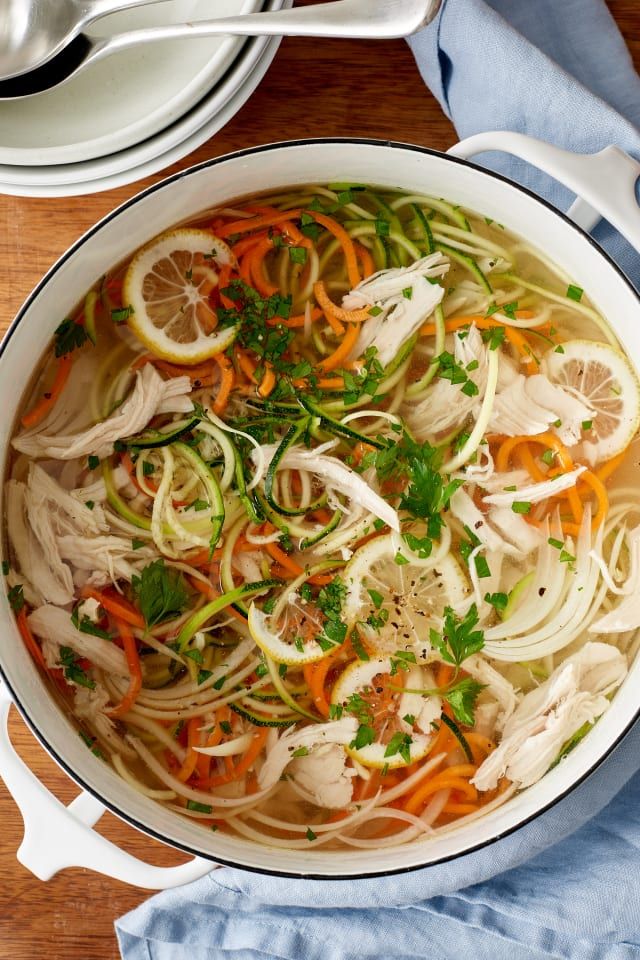 a pot filled with chicken, carrots and noodles on top of a wooden table